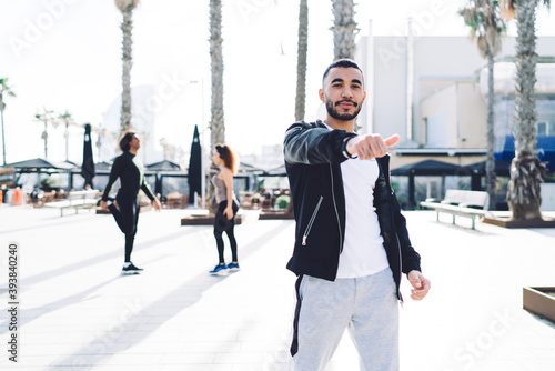 Half length portrait of handsome Hispanic trainer in sportive clothes showing OK while thumb up enjoying morning time for intensity workout, muscular successful male runner posing at urban street