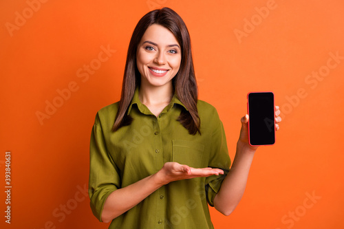 Photo portrait of smiling girl showing demonstrating empty space screen mobile phone isolated on vivid orange color background