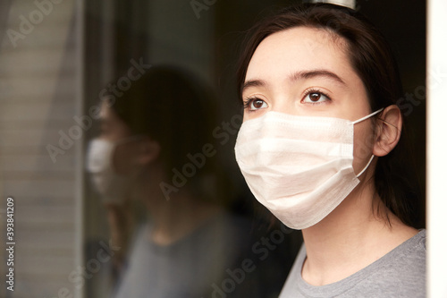 Portrait of a young girl in a protective medical mask, at the open door. The concept of isolating the population during the second wave of the coronavirus COVID-19. Selective focus, blurred background