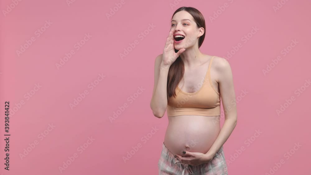 Fun young pregnant woman future mom in basic top stroking keeping hands on belly tummy with baby scream aside isolated on pastel pink background studio. Maternity family pregnancy gynecology concept Fun young pregnant woman future mom in basic top stroking keeping hands on belly tummy with baby scream aside isolated on pastel pink background studio. Maternity family pregnancy gynecology concept