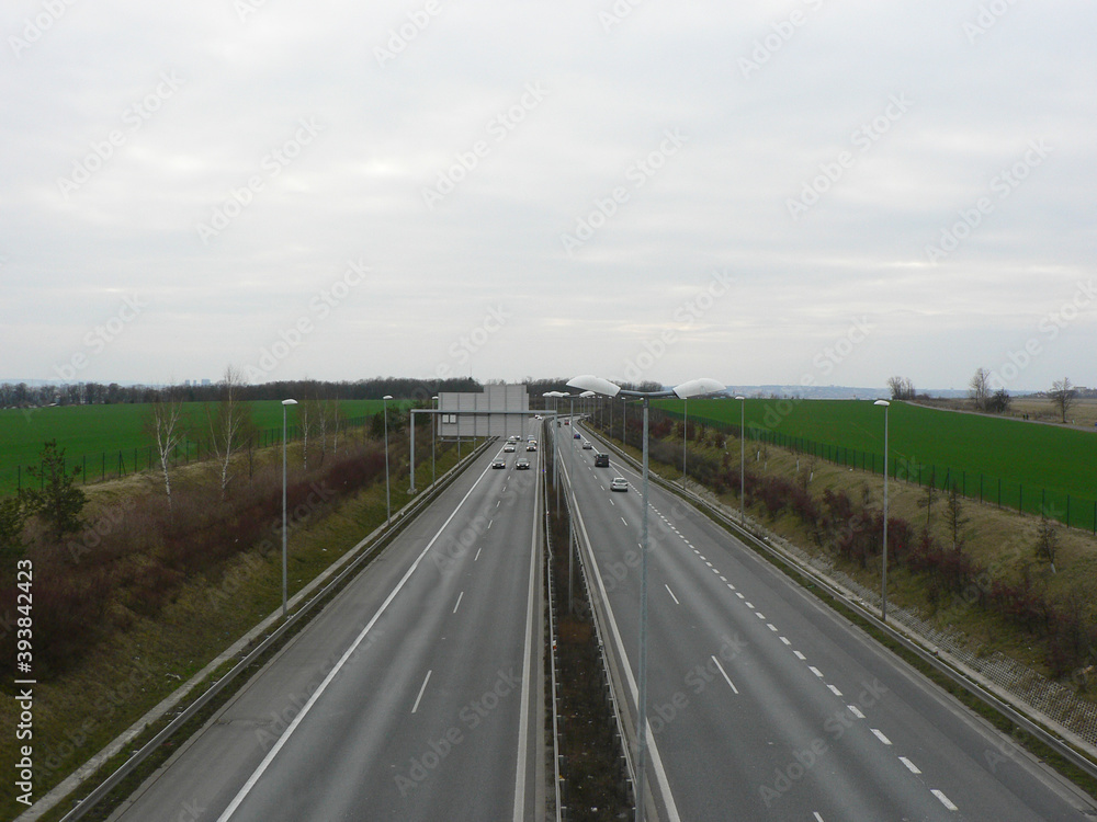 Empty highway on a cloudy day. A speeding car. View over the two-way road with two lanes in each direction. Green field along the road, autobahn or highway.