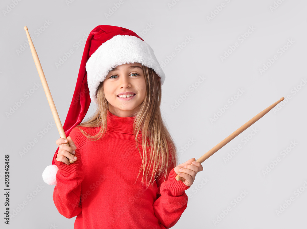 Cute little girl in Santa hat and with drumsticks on light background Cute little girl in Santa hat and with drumsticks on light background