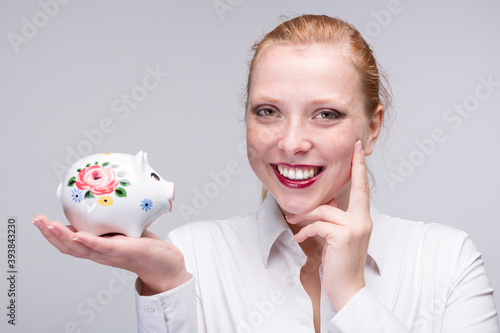 Young happy red haired woman presenting a piggy bank / porcelain bank in her hand