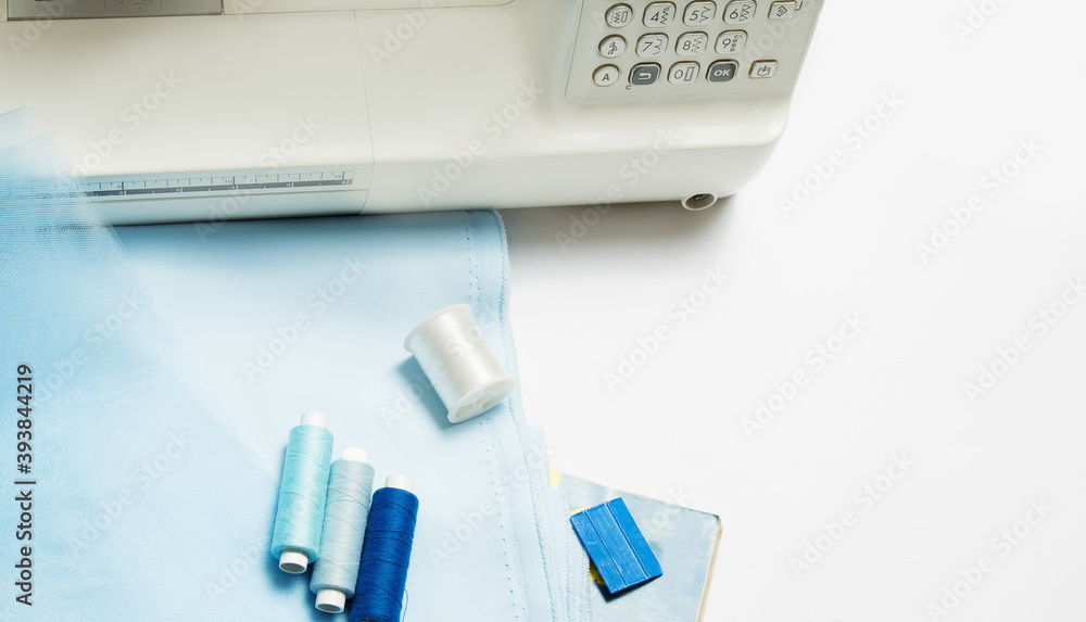 Sewing concept. Blue satin fabric and tulle with thread and, chalk and a sewing machine on a white background. top view. copy space Sewing concept. Blue satin fabric and tulle with thread and, chalk and a sewing machine on a white background. top view. copy space