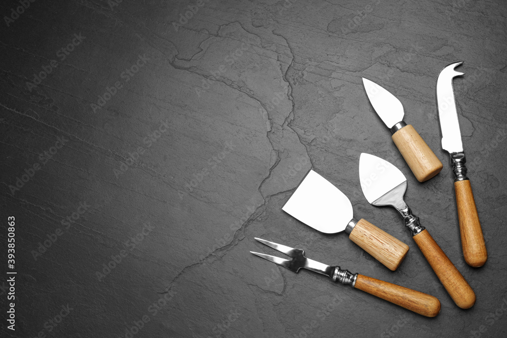 Cheese knives and fork on black stone table, flat lay. Space for text