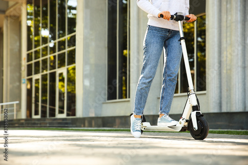 Obraz na płótnie Woman riding electric kick scooter outdoors. Space for text
