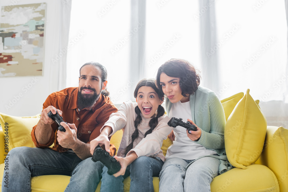 concentrated hispanic couple playing video game together with excited daughter