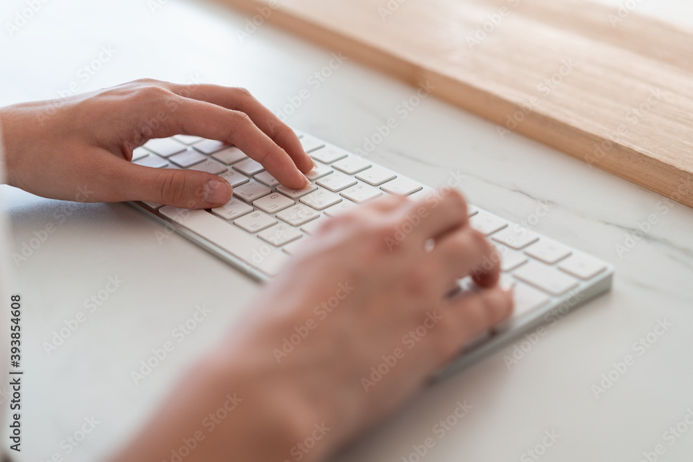 Woman hands, fingers typing on white wireless keyboard lying on marble office table desk, side view. Closeup of texting a letter, no face. Concept of work - obrazy, fototapety, plakaty 