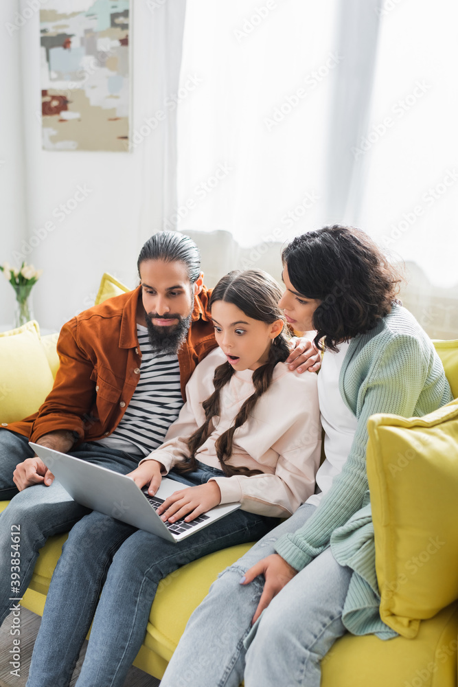 shocked hispanic girl watching film on laptop with family