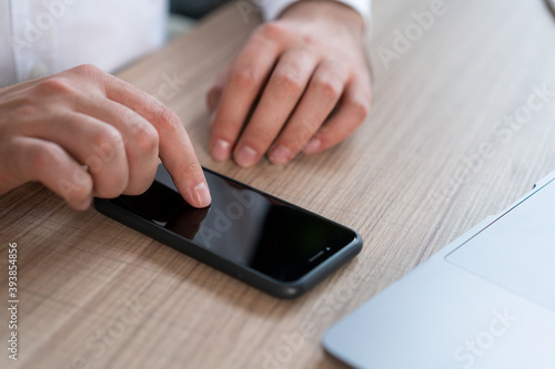 Closeup of male office manager typing on black phone screen, lying on wooden office table desk. Man hands with phone searching for information, no face. Concept of phone