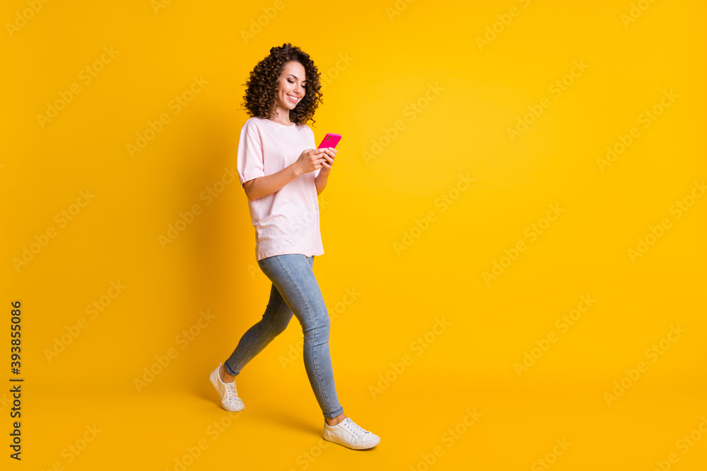 Full length body size photo of female millennial using app mobile phone walking isolated on vibrant yellow color background with copyspace
