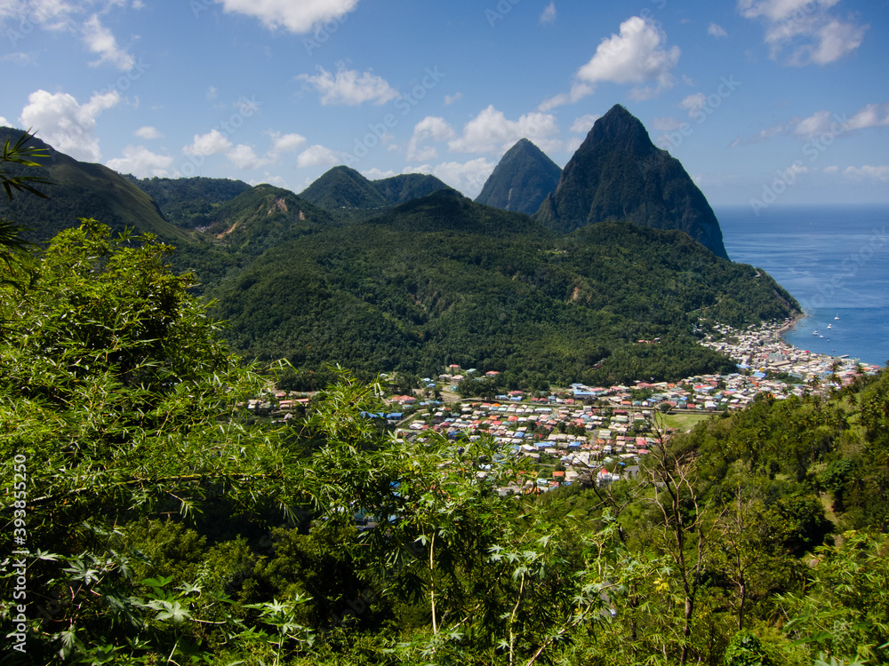 The Two Pitons mountains named Gros Piton and Petit Piton on the coast of St Lucia with a blue ocean and the homes and houses of the island in foreground with forested hillsides