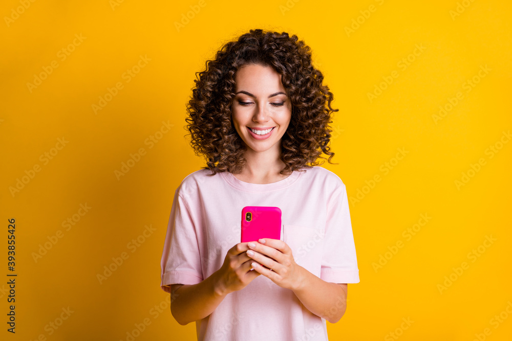 Photo portrait of woman smiling holding phone in two hands isolated on vivid yellow colored background Photo portrait of woman smiling holding phone in two hands isolated on vivid yellow colored background