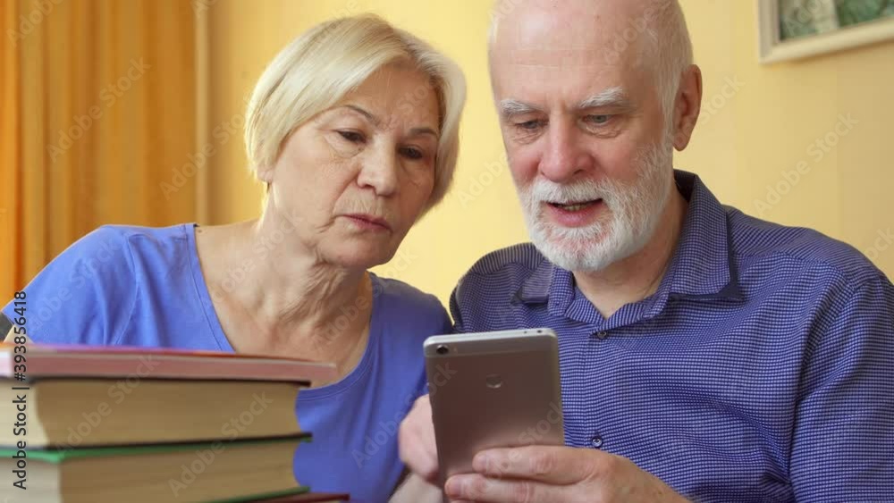 Senior couple learn foreign language via cellphone. Male student stay home and prepare to exam with mobile phone app. Active life after retirement. Concept of online education among elderly people Senior couple learn foreign language via cellphone. Male student stay home and prepare to exam with mobile phone app. Active life after retirement. Concept of online education among elderly people