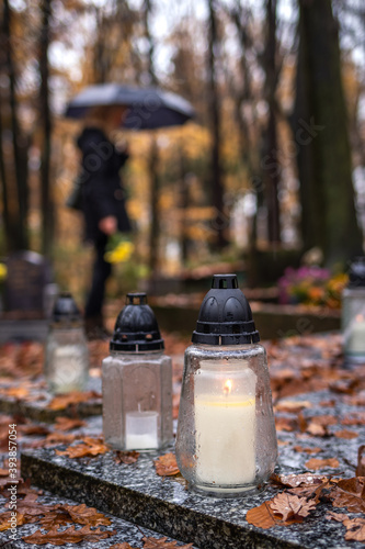 Grave candle lantern at tombstone and mourning woman with umbrella in cemetery