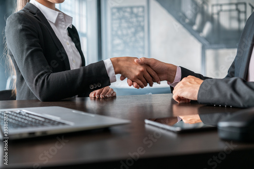 Woman and man handshake in office business room, no face. Business partners, female and male in black jackets shaking hands, concept of agreement