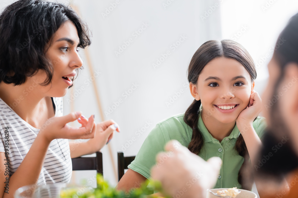 Hispanic girl smiling while looking at father near mother and cereals on blurred foreground