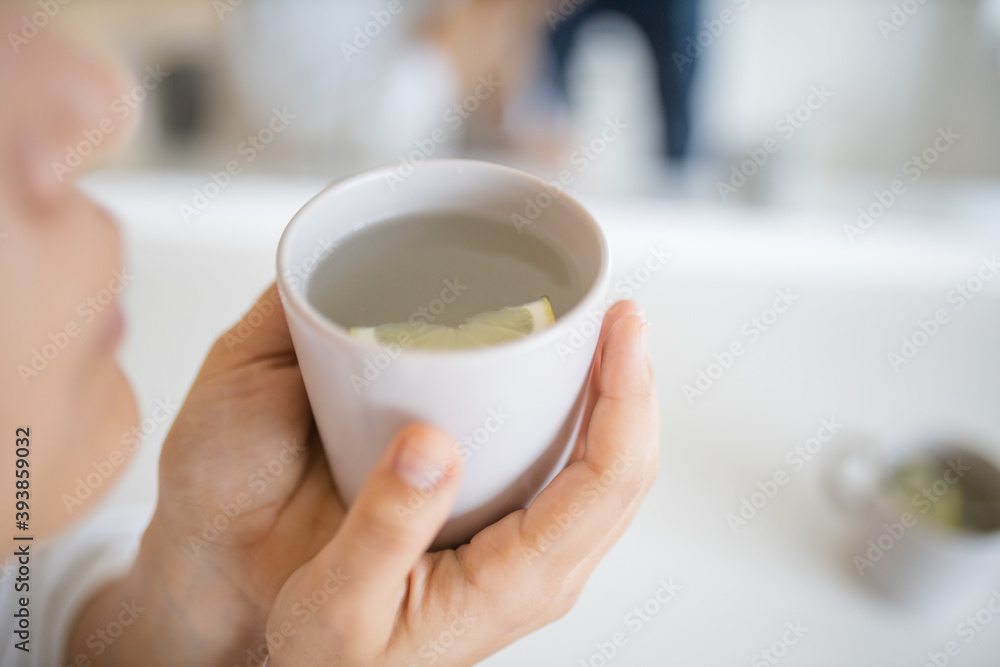 Woman gently blowing on a cup of lemon tea with a lemon slice inside Woman gently blowing on a cup of lemon tea with a lemon slice inside