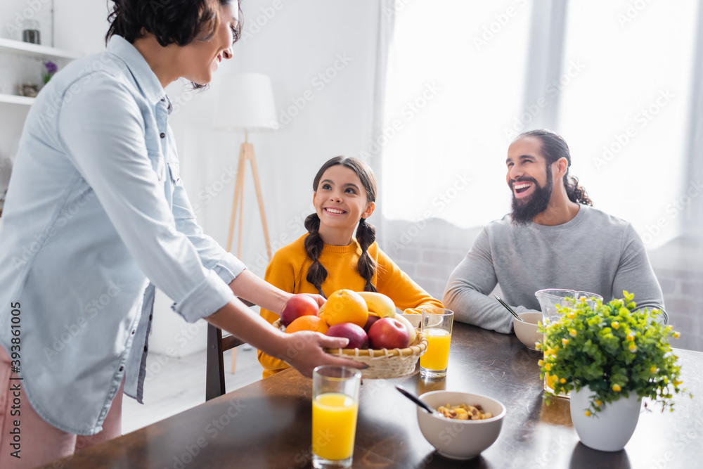 Smiling hispanic father and girl looking at mother with fruits in kitchen Smiling hispanic father and girl looking at mother with fruits in kitchen