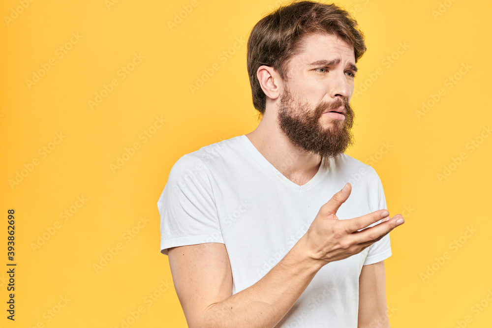 Man in white t-shirt emotions studio gestures with hands displeased facial expression yellow background Man in white t-shirt emotions studio gestures with hands displeased facial expression yellow background