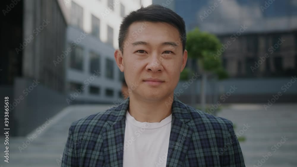 Smiling handsome young asian businessman standing look at camera outside near business center. Portrait successful career attractive manager handsome confident. Slow motion Smiling handsome young asian businessman standing look at camera outside near business center. Portrait successful career attractive manager handsome confident. Slow motion