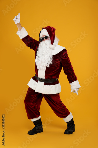 Santa Claus with headphones listening to Christmas music on yellow background © New Africa