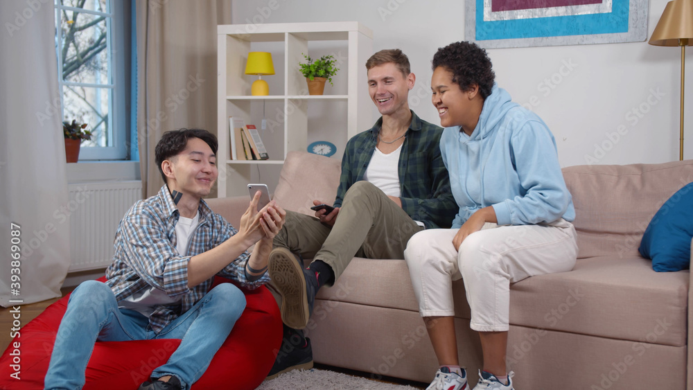 Young happy multicultural people in casual wear looking at smartphone and laughing Young happy multicultural people in casual wear looking at smartphone and laughing