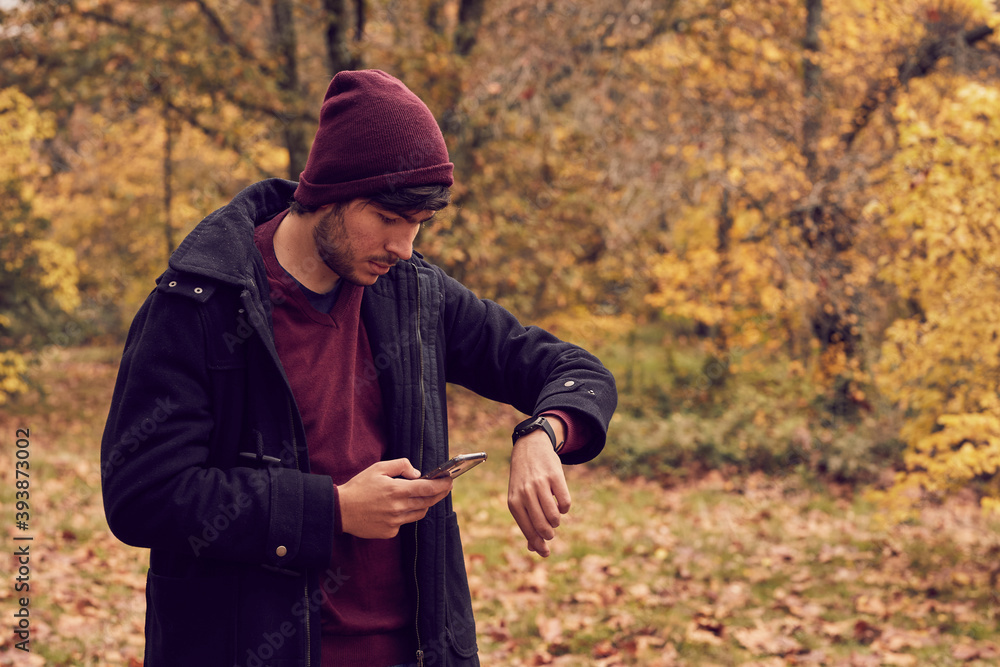 Chico mirando el reloj y el móvil en un parque en otoño