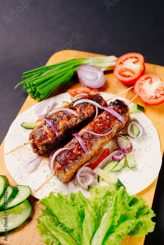 Grilled lula kebab on pita bread with vegetables on a dark background