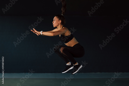 Side view of female athlete jumping in gym, warming up her body