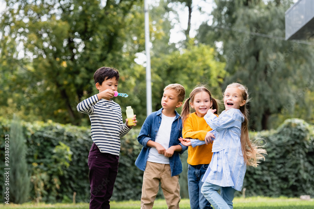 Cheerful multiethnic kids with soap bubbles standing in park Cheerful multiethnic kids with soap bubbles standing in park