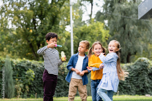 Cheerful multiethnic kids with soap bubbles standing in park