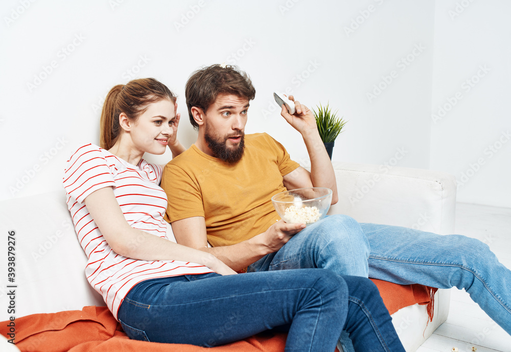 Fun man and energetic woman watching TV on the couch popcorn in a plate family communication Fun man and energetic woman watching TV on the couch popcorn in a plate family communication