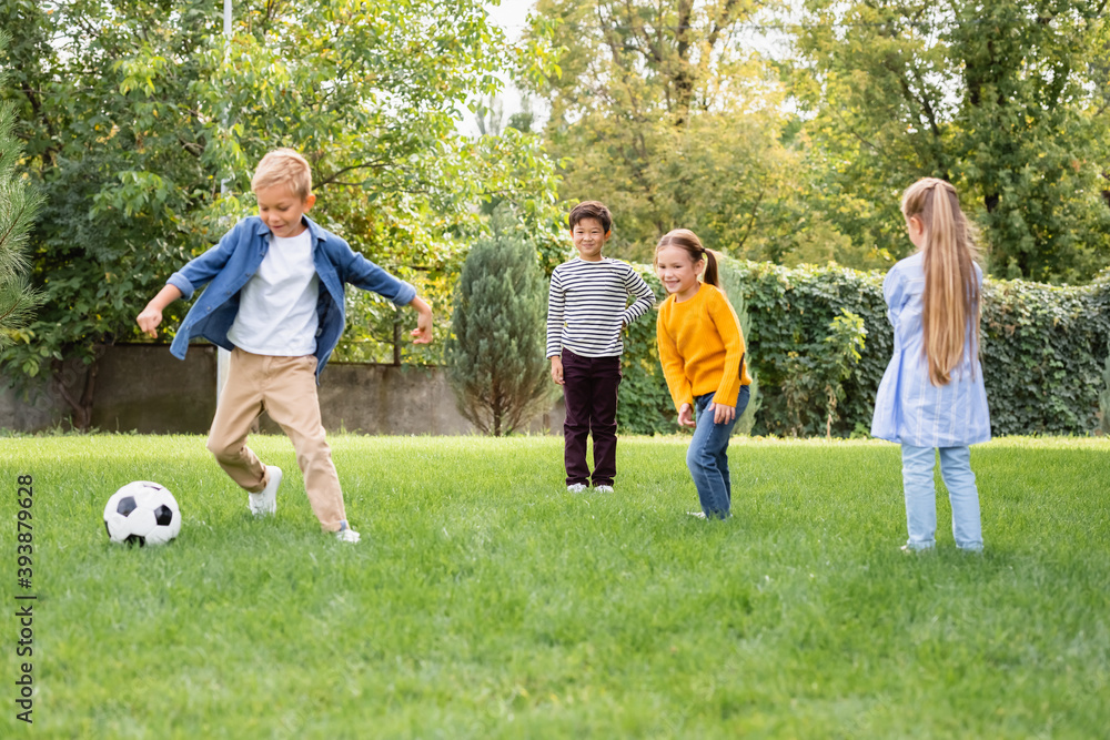 Obraz premium Positive multiethnic children standing near friend playing football in park