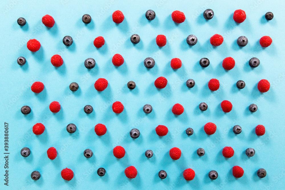 Fresh raspberries and blueberries alternately arranged on blue background. Little colorful berries organized on turquoise paper. Color table full of small heatlhy sweet fruit. Fresh raspberries and blueberries alternately arranged on blue background. Little colorful berries organized on turquoise paper. Color table full of small heatlhy sweet fruit.
