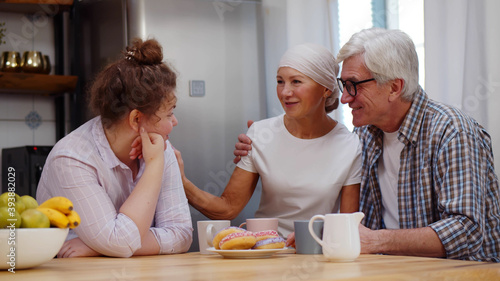 Adult daughter and senior husband supporting woman with cancer having coffee together at home