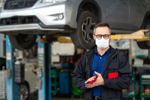 Portrait of caucasian man Cleaning Hands With Cloth and wearing medical face mask protection coronavirus.. Expertise mechanic working in automobile repair garage.