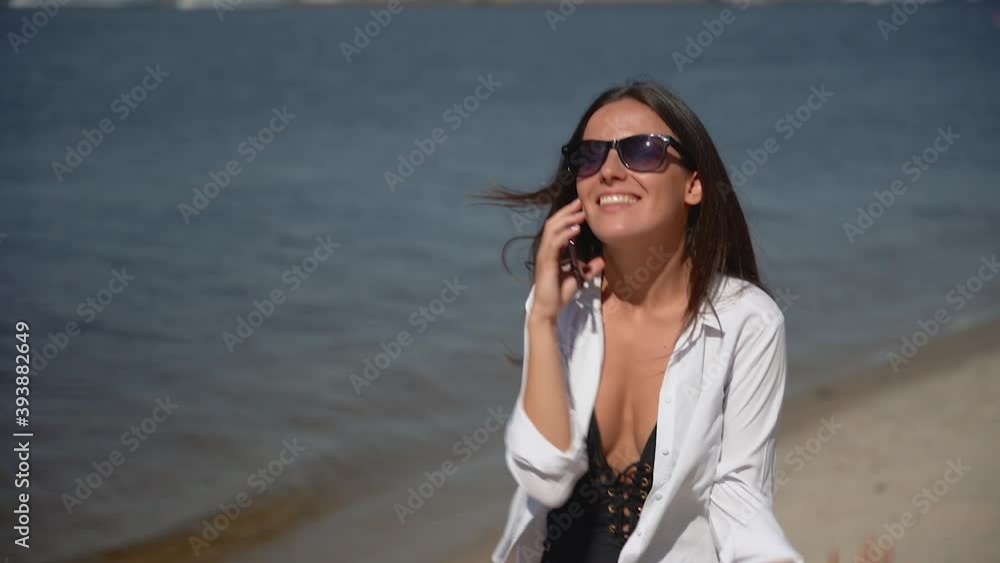 Young pretty woman talking on the phone and walking along the seashore. Happy female on vacation at the beach. Young pretty woman talking on the phone and walking along the seashore. Happy female on vacation at the beach.