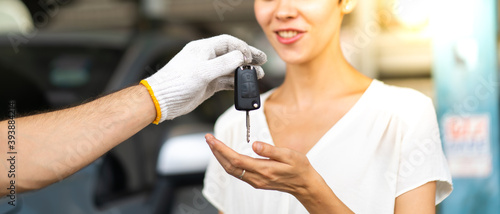 Middle age mechanic man with beard gives the car key to female customer at Car maintenance station and automobile service garage
