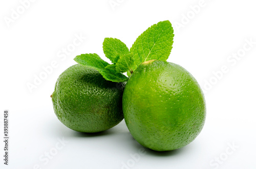 Closeup of two ripe juicy limes and green mint leaves on the white background