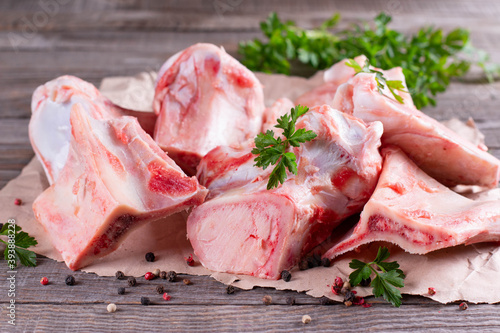 Foto Fresh beef bone on wooden background with vegetables and herbs on the background