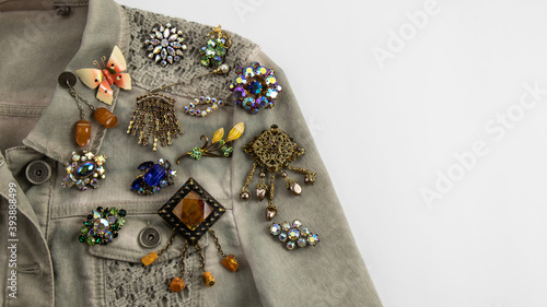 Fotografija Many wonderful multi colored vintage brooches with sparkling gems, crystals and amber are  pinned on a light gray denim jacket