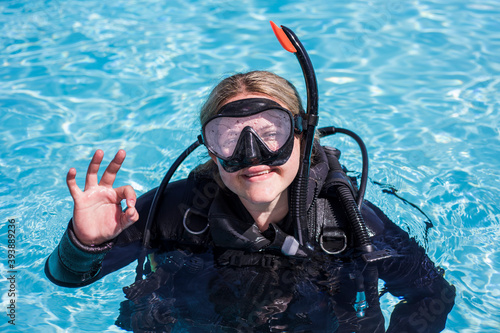Scuba diver in a pool with her dive mask on looking at the camera smiling and showing the ok sign.