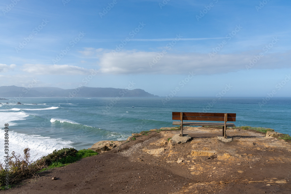 scenic viewpoint with wooden bench on beautiful ocean coast with high cliffs and big waves