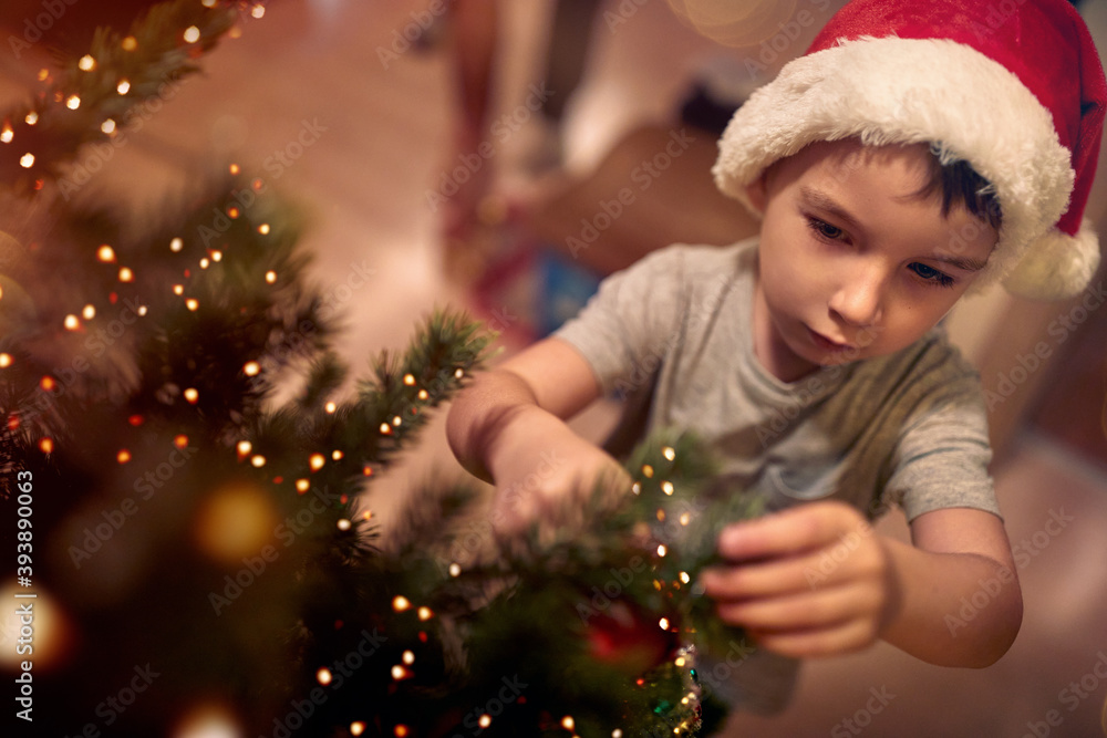 A little kid focused on ornamenting a Christmas tree at home. Together, New Year, family, celebration A little kid focused on ornamenting a Christmas tree at home. Together, New Year, family, celebration