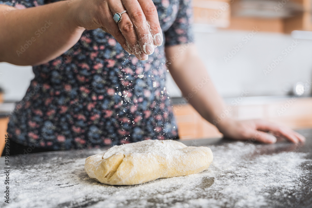 Woman sprinkling dough with flour in kitchen.