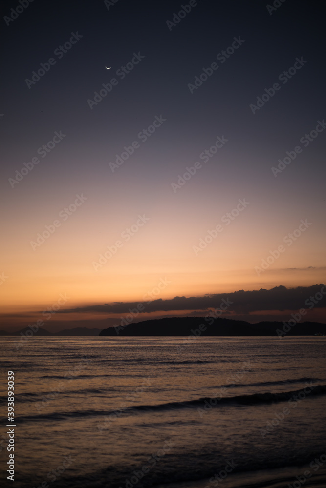 view of sea from beach land the water reflecting the blue and orange sky dark at evening night with an island or peninsula in the background horizon