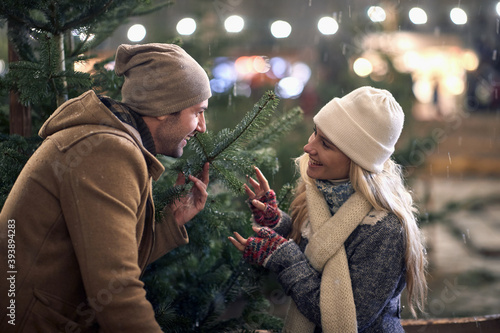 A young couple in love having good time viewing a christmas tree on a snowy weather in the city. Christmas tree, love, relationship, Xmas, snow