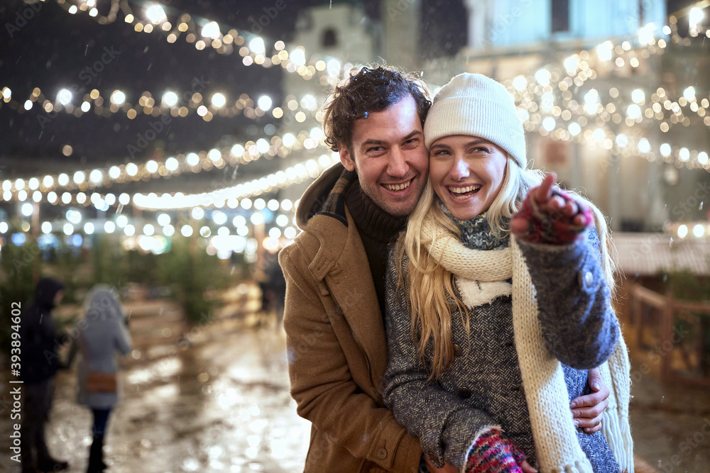 A young couple in love posing for a photo at christmas festival on a snowy weather in the city. Festival, love, relationship, Xmas, snow