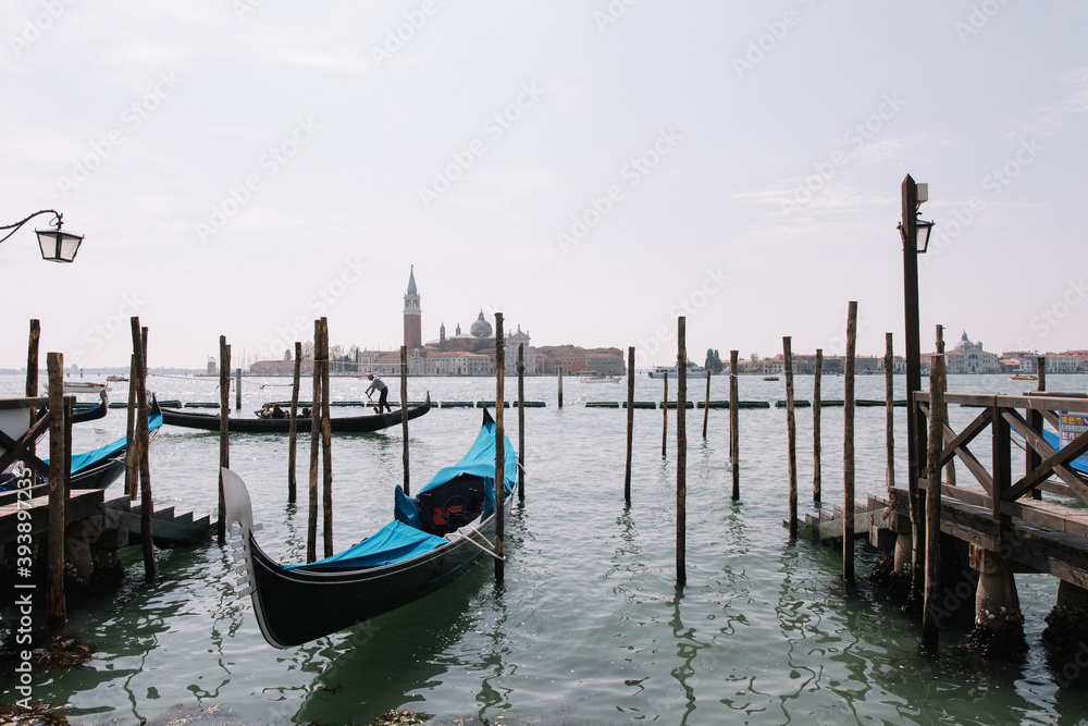 view of old wooden docks on the lake canal in venice during summer easter of boats yachts ships man working and island old town on the other side